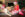blond in santa hat holding a red KONG out to a laying down gold dog