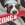 A white and brown dog holding a red KONG stick in its mouth.