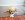 Un cucciolo biondo sdraiato all'interno su un tappeto grigio, che mastica un giocattolo per cani in corda KONG blu e bianco.